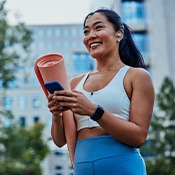 Smiling woman walking on park with workout mat