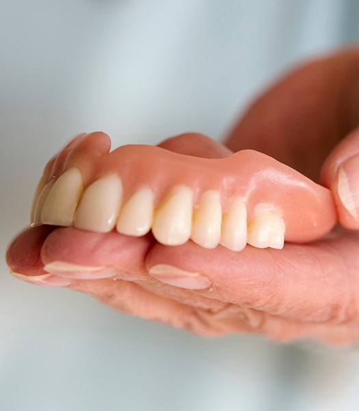 Close-up of hand holding dentures in Los Angeles, CA