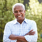 Senior man smiling outside with arms folded