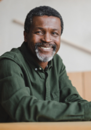 Older man in dark green shirt smiling while sitting at desk