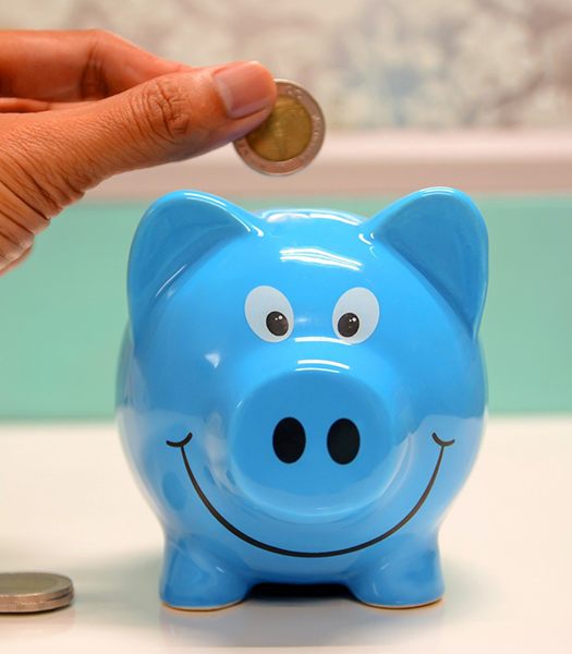 Hand putting coin in blue piggy bank